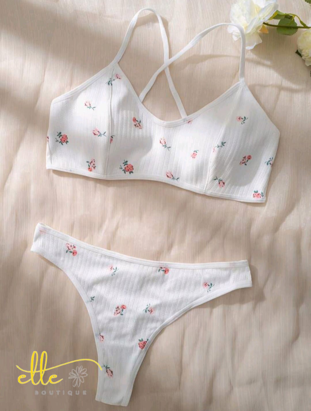 A charming and cozy two-piece set crafted from a comfortable ribbed knit fabric. It features a delicate all-over floral print, a wide underband bralette with crisscross back straps, and a matching thong panty for soft, everyday comfort.